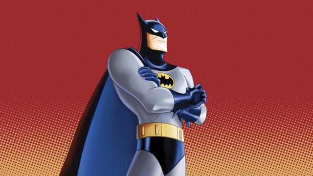 Batman stands with his arms crossed in front of a red background.