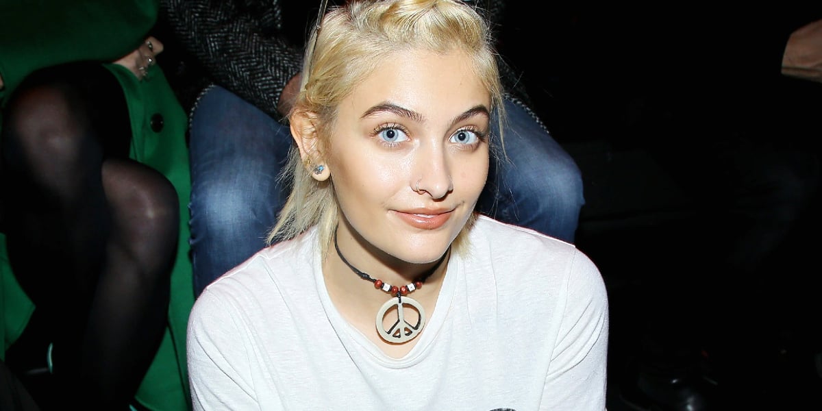 Paris Jackson is seen wearing a peace sign necklace and smiling. 