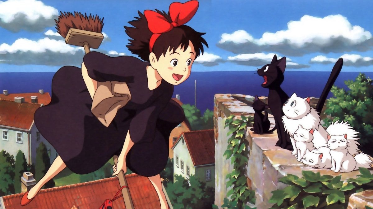 A girl riding a broomstick looks over happily at a black cat.
