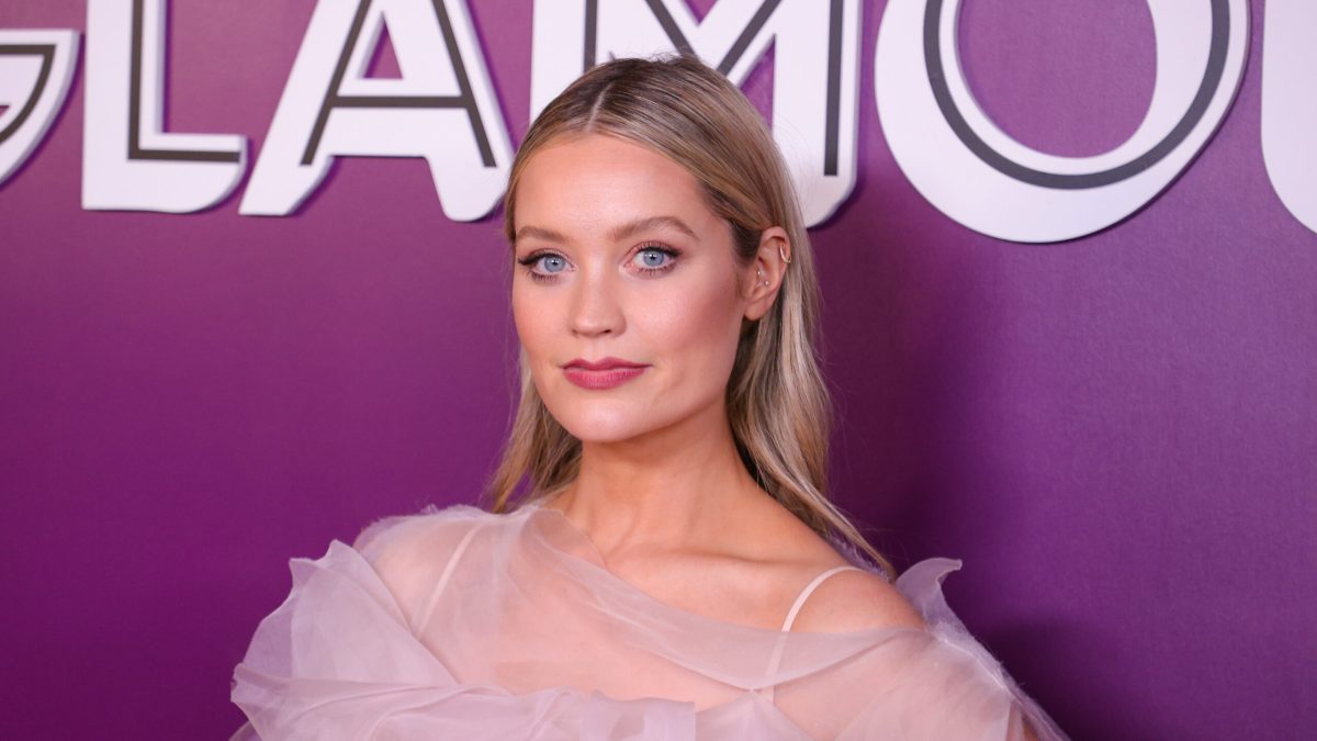 A shoulders up portrait of Whitmore in a diaphanous pink dress in front of a purple background