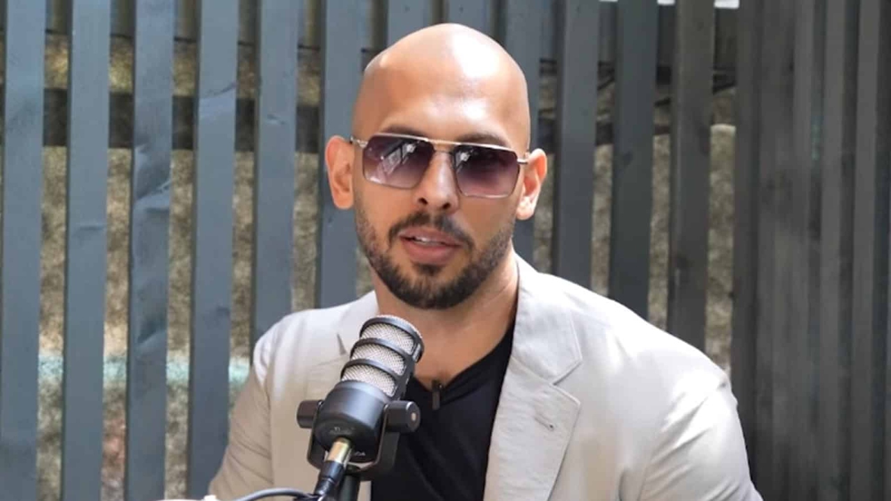 Andrew Tate wearing sunglasses seated behind a microphone