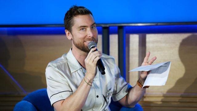 Lance Bass smiles into the camera while speaking into a mic