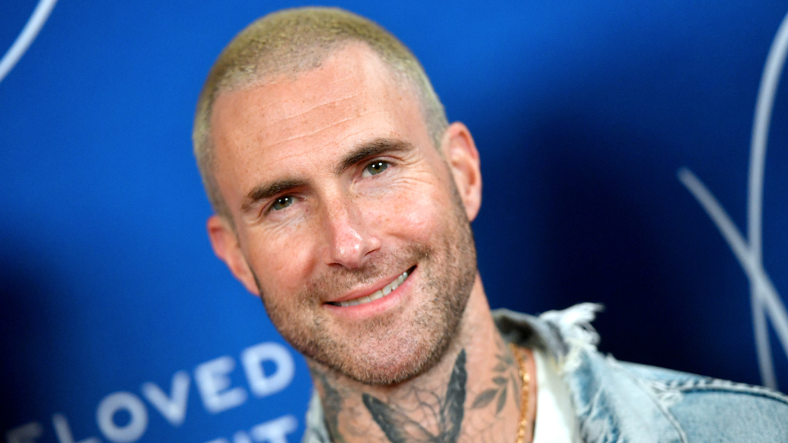 Close up shot of Adam Levine sporting a blonde buzz cut and neck tattoos