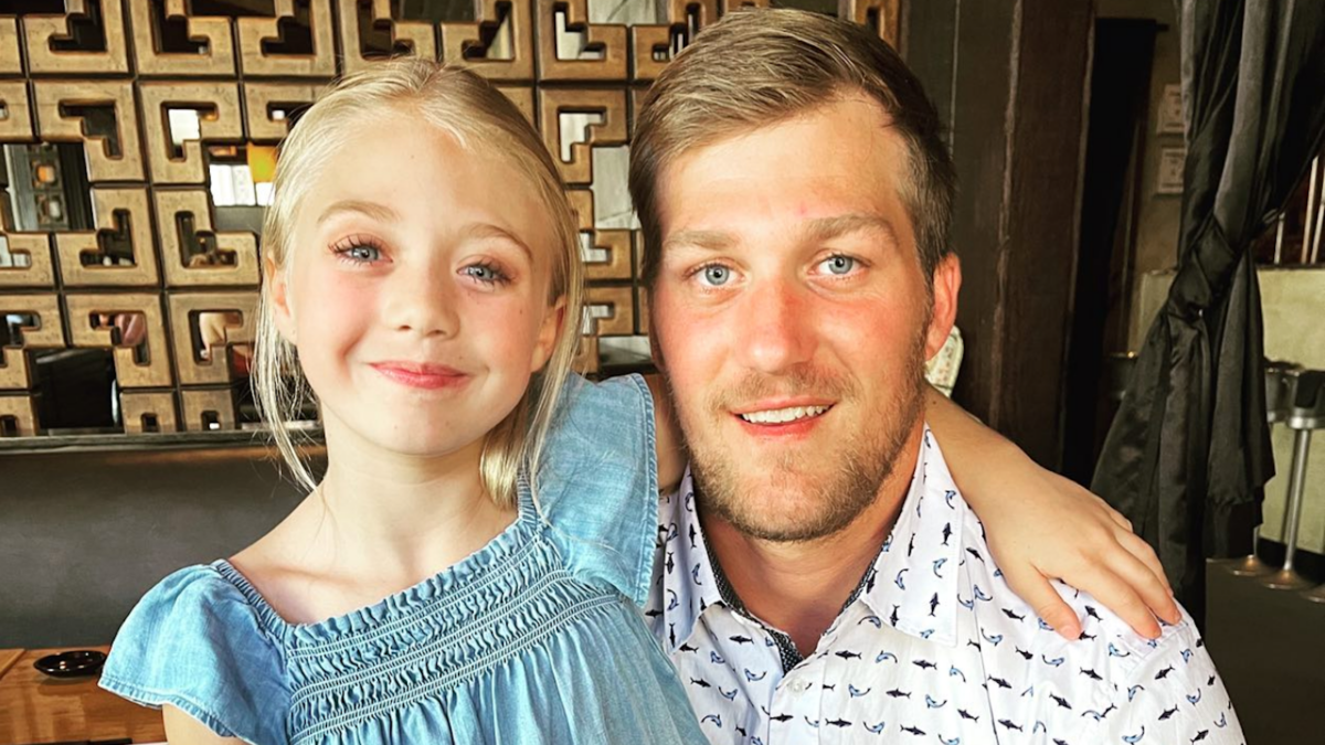 Everleigh Rose in a blue dress sitting on her father Tommy Smith's lap, arm wrapped around his shoulder