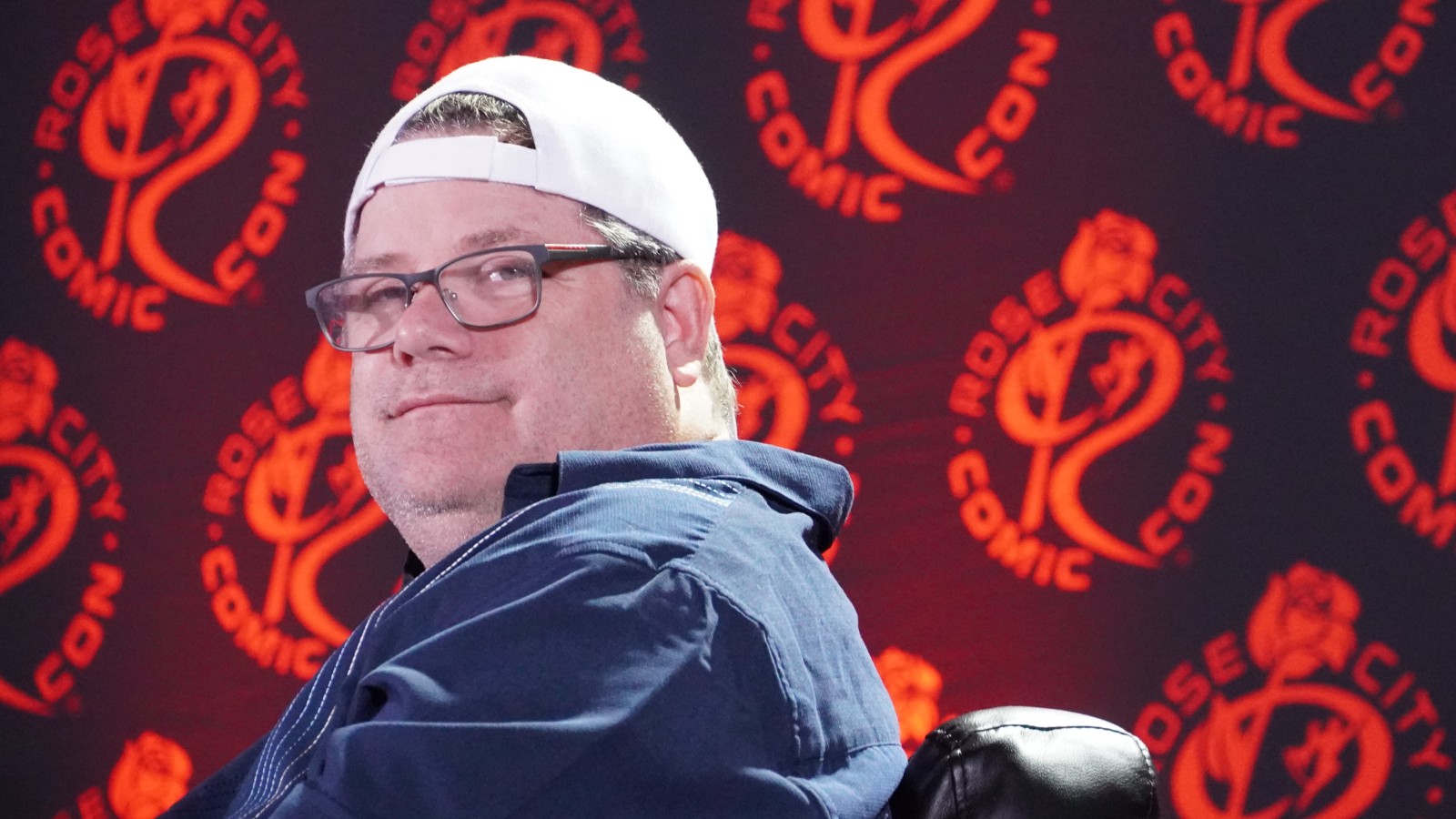 Sean Astin listens to a fan's question during a Q&A panel against a red background.