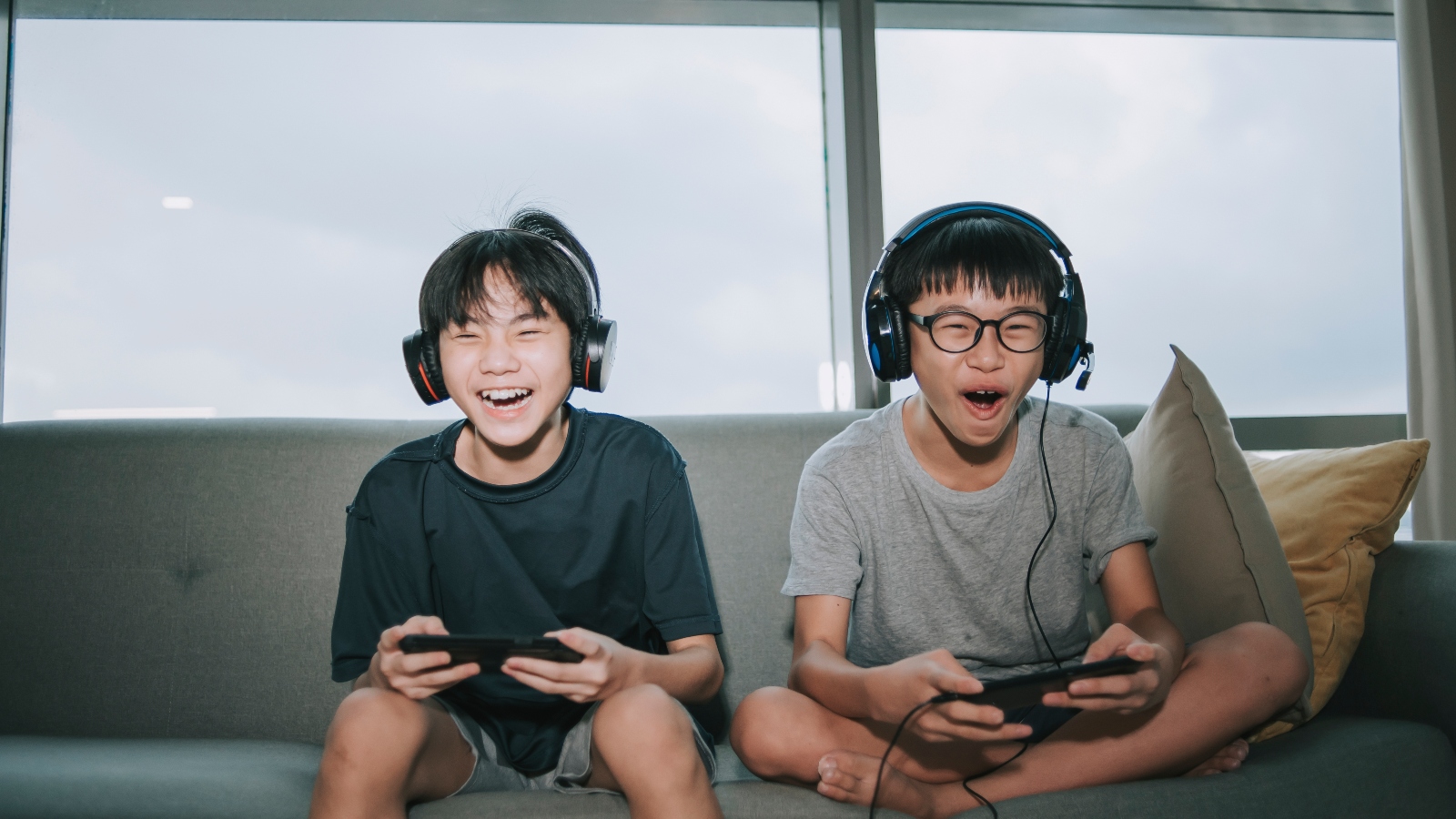 Two Asian brothers playing video games on a sofa