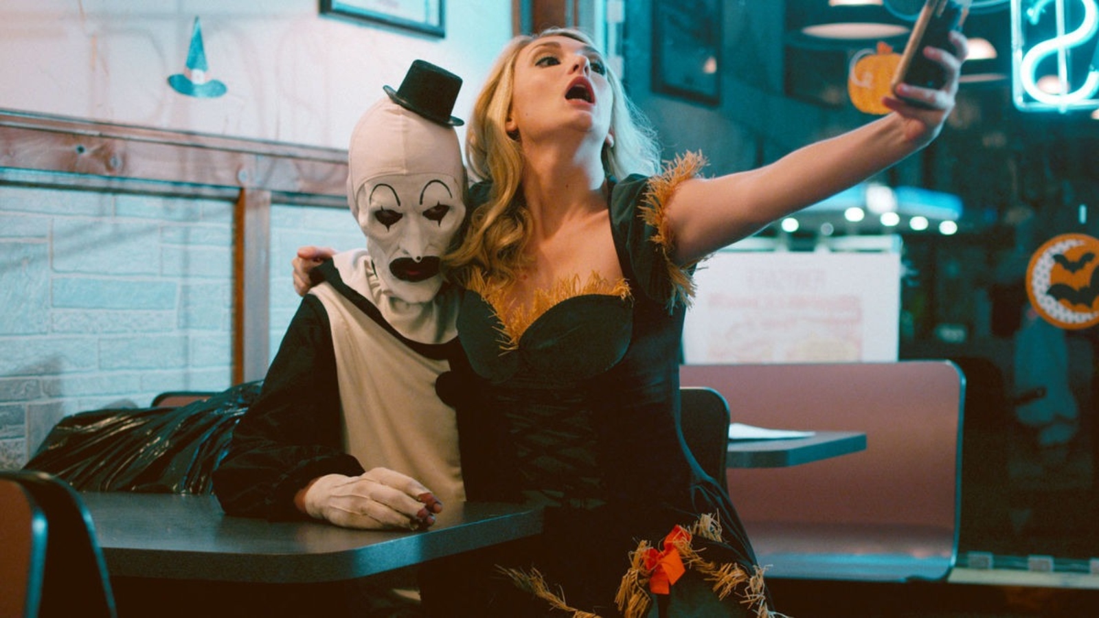 Art the Clown and Dawn from Terrifier are taking a selfie in a restaurant. 