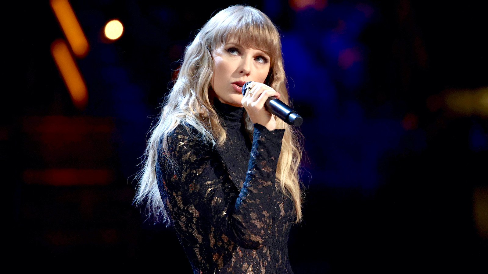 Taylor Swift in all black holding a microphone on stage