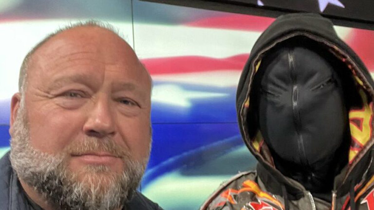 Alex Jones poses with Kanye West, who is wearing a black mask covering his entire face.