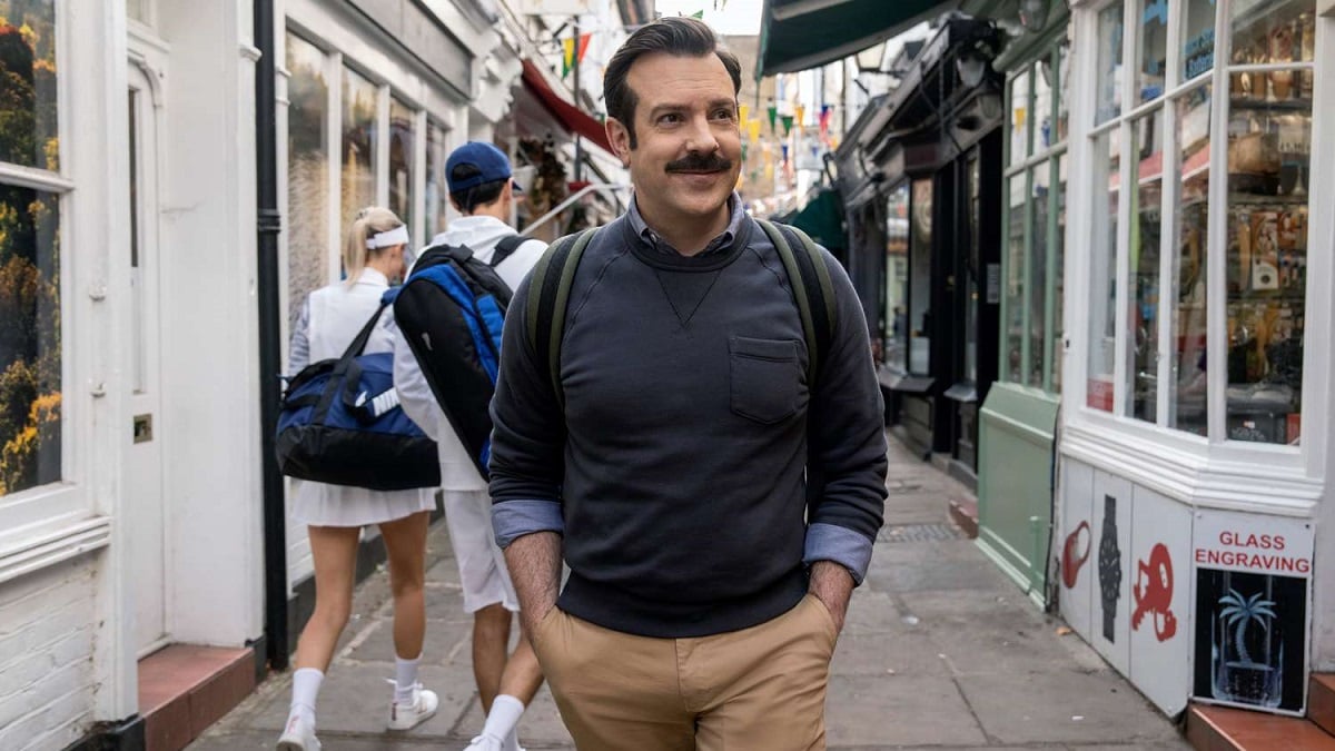 Ted Lasso is walking down the street with a backpack on. 