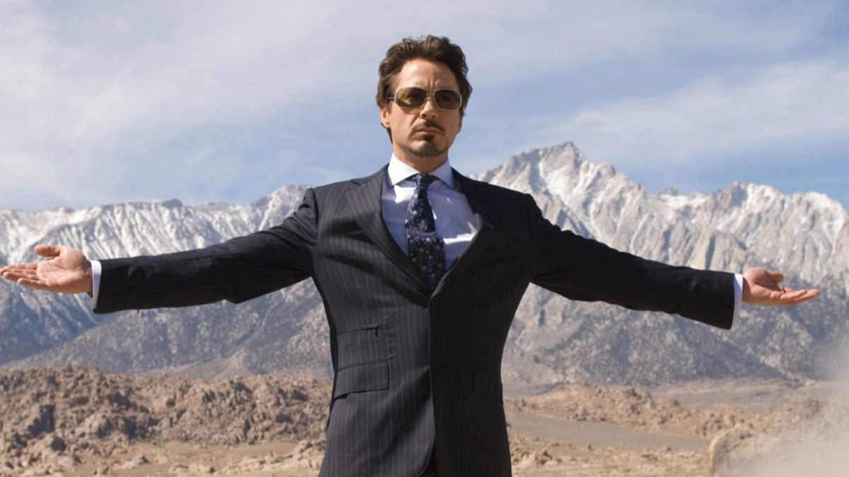 Robert Downey Jr.'s Tony Stark stands with his arms spread against a middle eastern desert in a screenshot of a famous moment from 2008's Iron Man. 