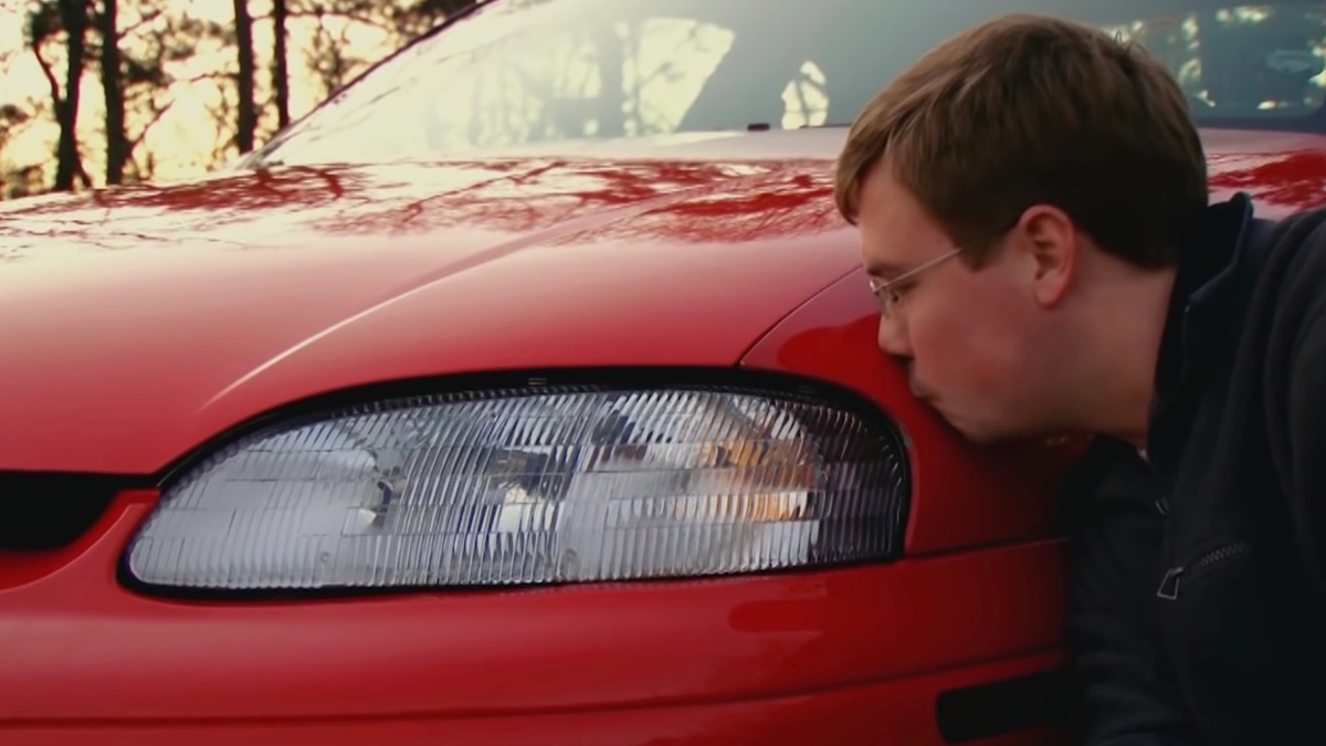 a man passionately kisses his red car.