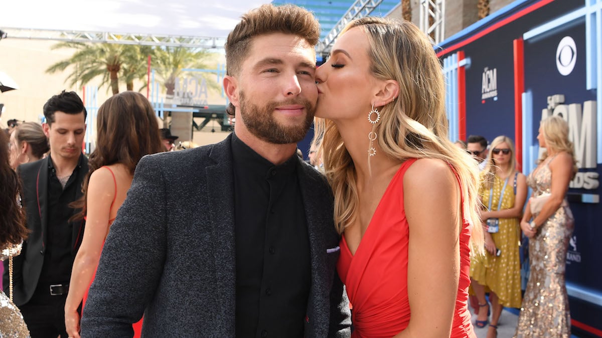 Lauren Bushnell in a red dress and Chris Lane in a black suit on the red carpet as Lauren plants a kiss on Chris' cheek