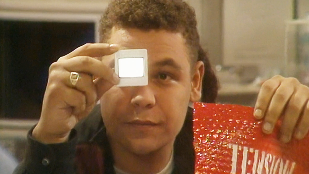 Lister stars at a film slide while clutching a red piece of packaging plastic labeled 'Tension Sheet.' 