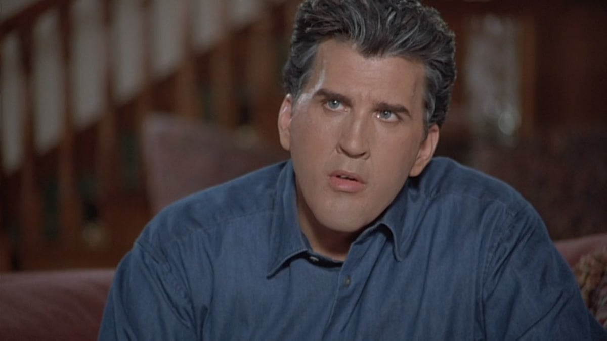 Daniel Roebuck as Jay Leno in the movie 'The Late Shift' listens intently while seated on a couch and wearing a blue button-up shirt.