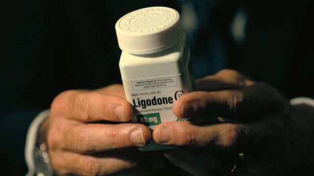 Up-close shot of a man holding a prescription bottle of a medication called Ligadone.
