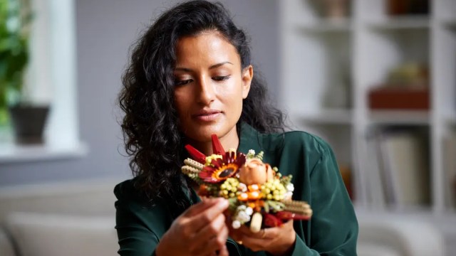 A woman with brown curly hair holds a completed LEGO project with a Thanksgiving theme