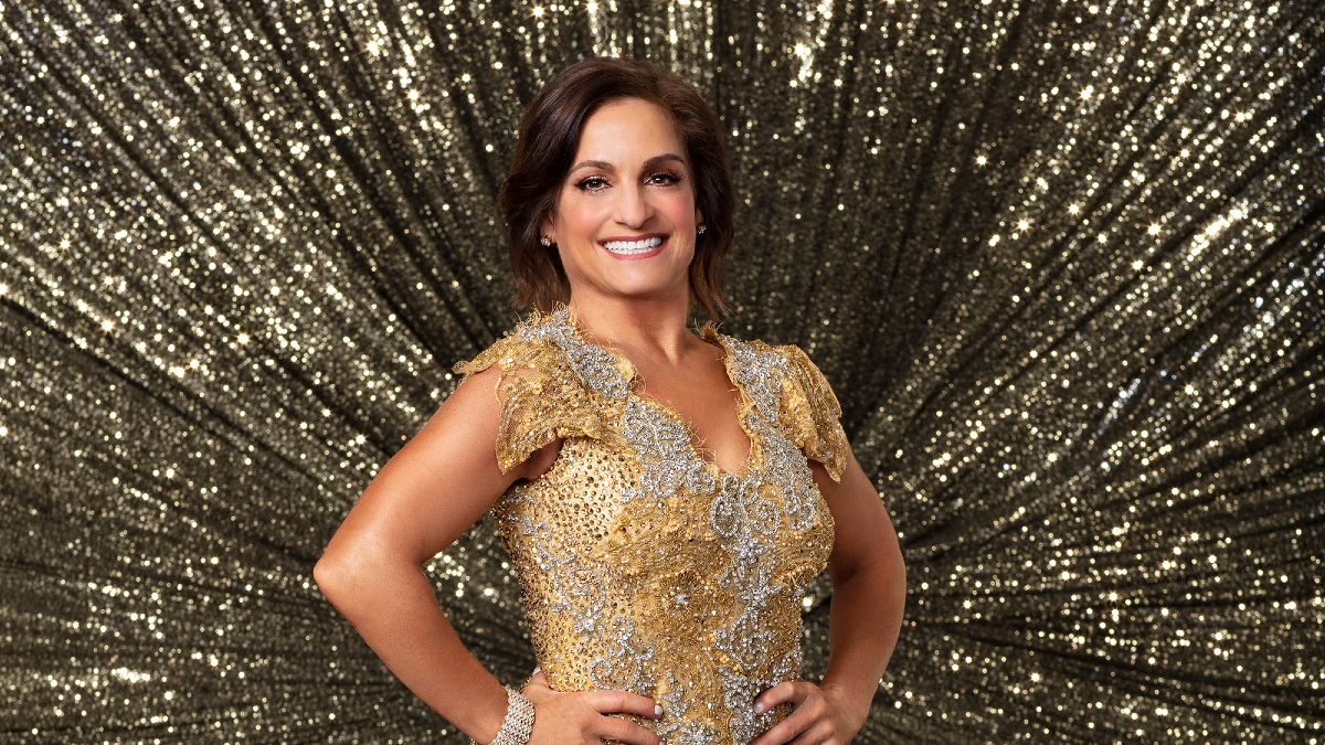 Mary Lou Retton is a sparkling golden dress in front of an equally golden sparkly backdrop.