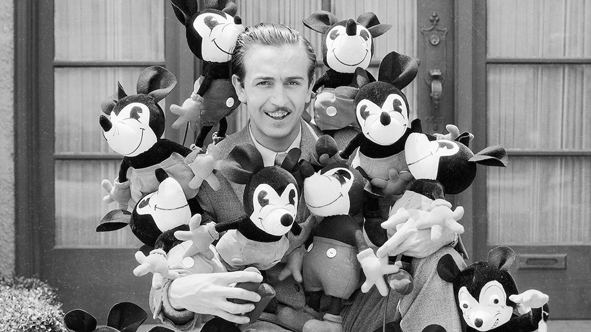 Walt Disney poses with many Mickey Mouse stuffed toys.