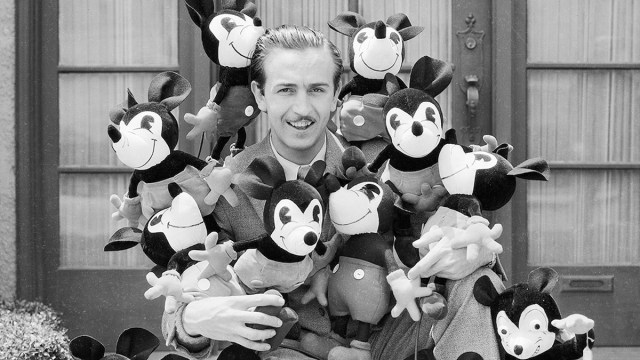 Walt Disney poses with many Mickey Mouse stuffed toys.