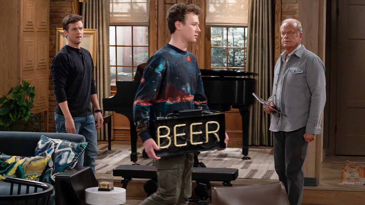 An exasperated Frasier (Kelsey Grammer) and Freddy (Jack Cutmore-Scott) look on as David (Anders Keith) brings a 'BEER' sign into the apartment. 