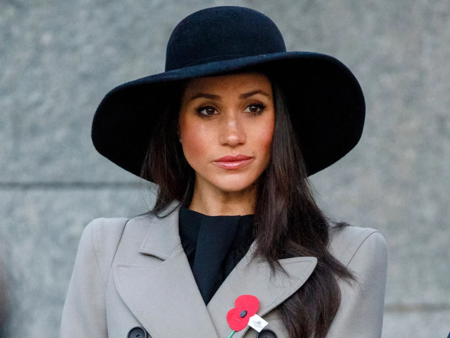 Meghan Markle is wearing a black hat and looking into the distance.
