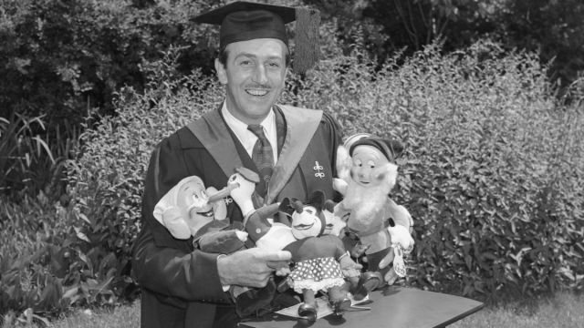Walter E. Disney, famous producer of animated cartoons, is shown with doll replicas of his most famous characters which were responsible for his being conferred an honorary degree of Bachelor of Arts at Harvard University Commencement.