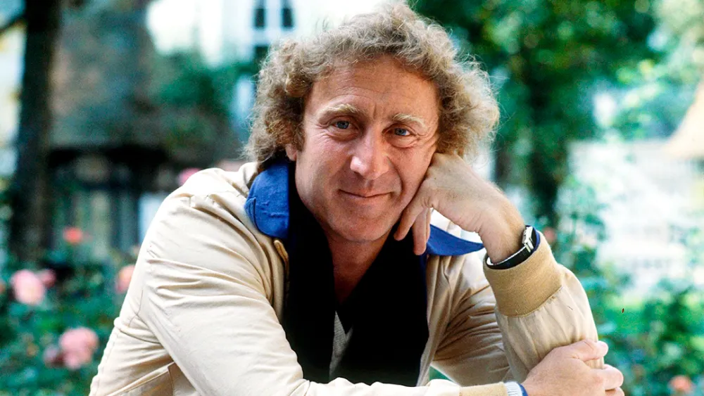 Gene Wilder is resting his head on his hand and smiling for a picture.