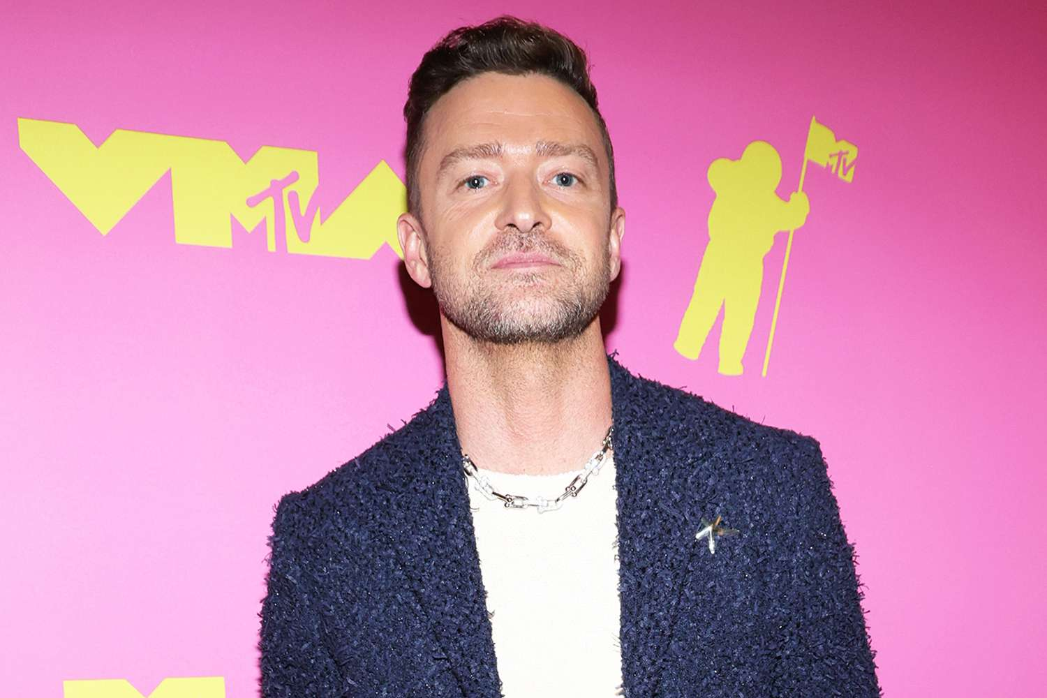 Justin Timberlake is standing in front a pink wall at an awards show.