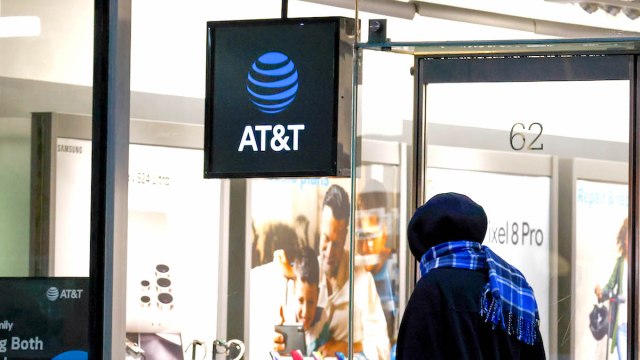 A person in a black hoodie and blue scarf looking into an AT&T store in New York City, 2024.