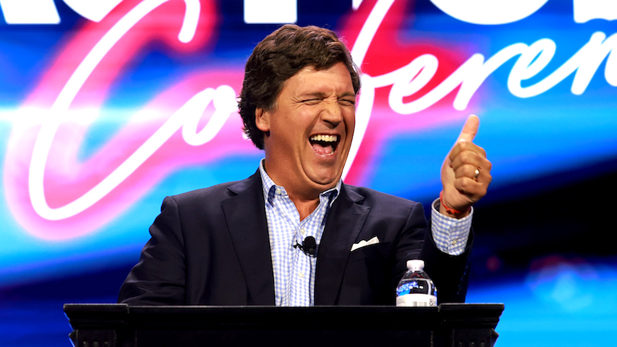 Tucker Carlson laughing and giving a thumbs-up at the Turning Point Action conference