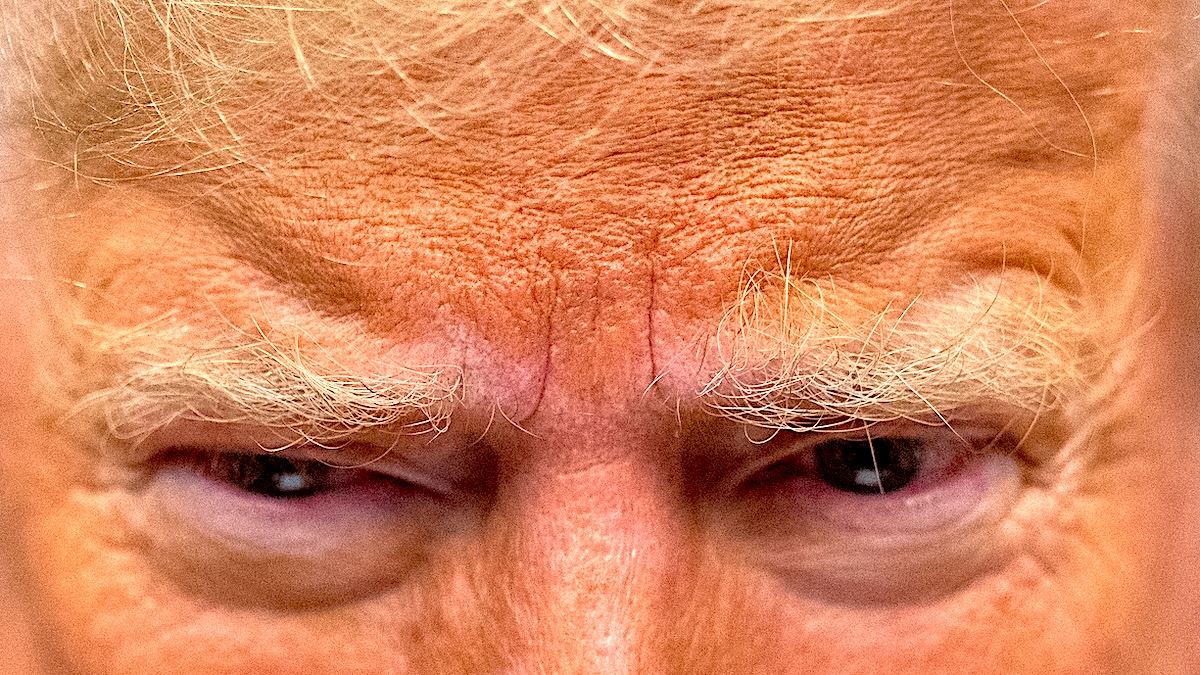 A close-up of Donald Trump's angry eyebrows and chalky, orange-makeup face