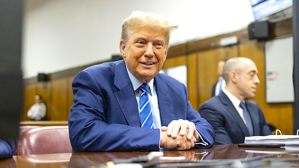 Donald Trump smiling in orange makeup and a blue suit in court in 2024