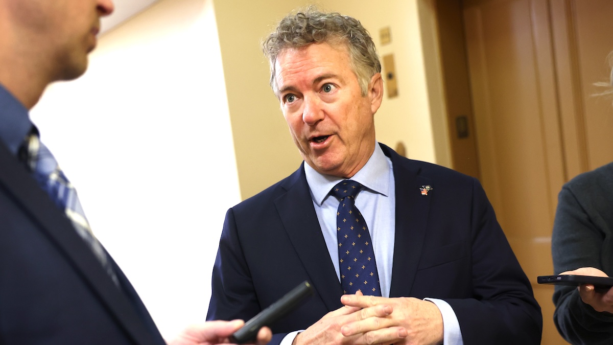 Rand Paul in a navy suit and tie talking to someone with his fingers intertwined