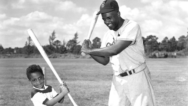 Jackie Robinson, (1919-1972), the baseball star, is shown here teaching his son Jackie Jr. how to bat.