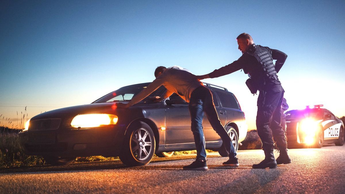 A Professional Middle Aged Policeman Performing a Pat-Down Search on a Fellon With his Hands on Car Hood. Documentary-like Shot of Procedure of Arresting Suspects. Experienced Cop Looking for Weapons