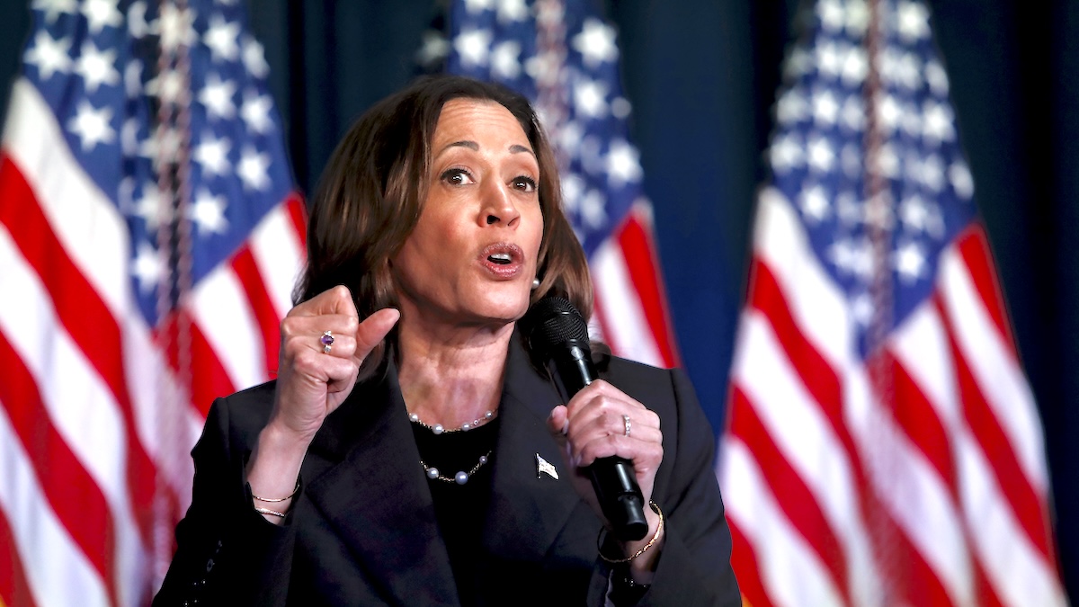 Kamala Harris speaking in a black suit with American flags behind her