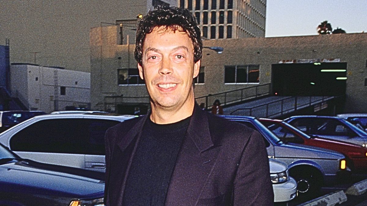 British actor and singer Tim Curry wearing a black jacket over a black crew neck top, walking beside a parking lot, United States, circa 1992.