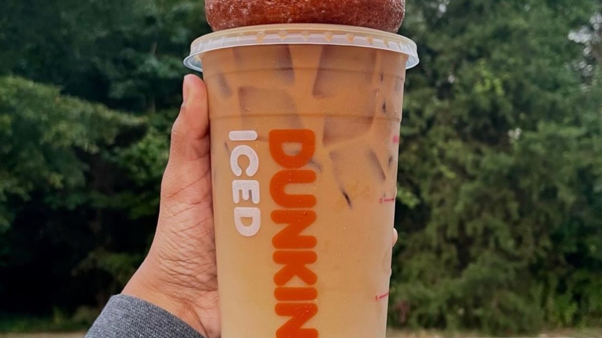 Someone's hand holding up an iced coffee and donut from Dunkin' Donuts